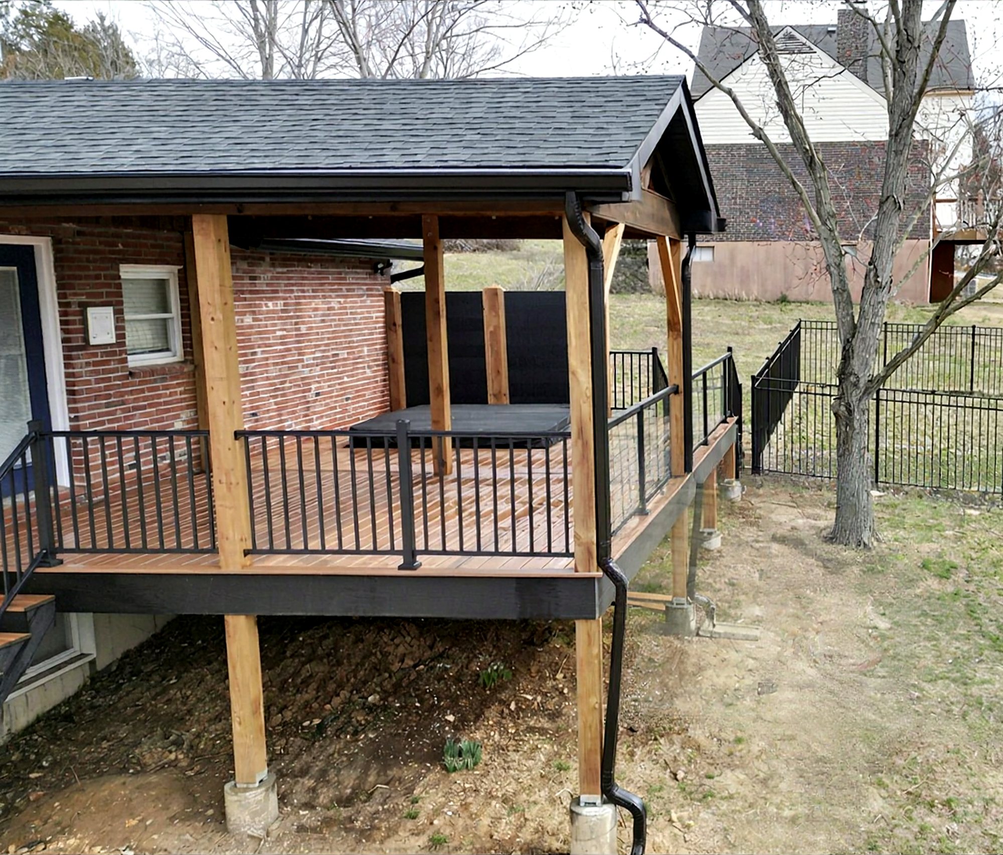 Covered deck with cedar posts and black railings, hot tub behind a privacy screen