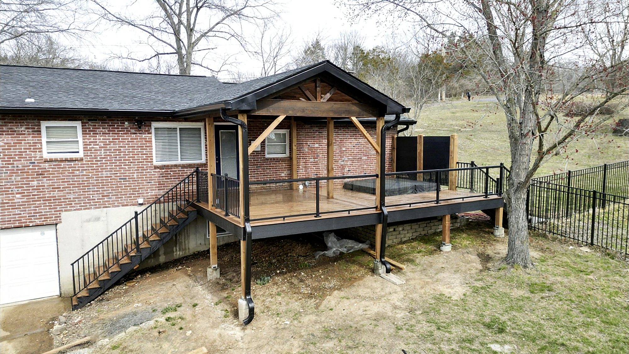 Covered deck with a hot tub, privacy screen and black railings